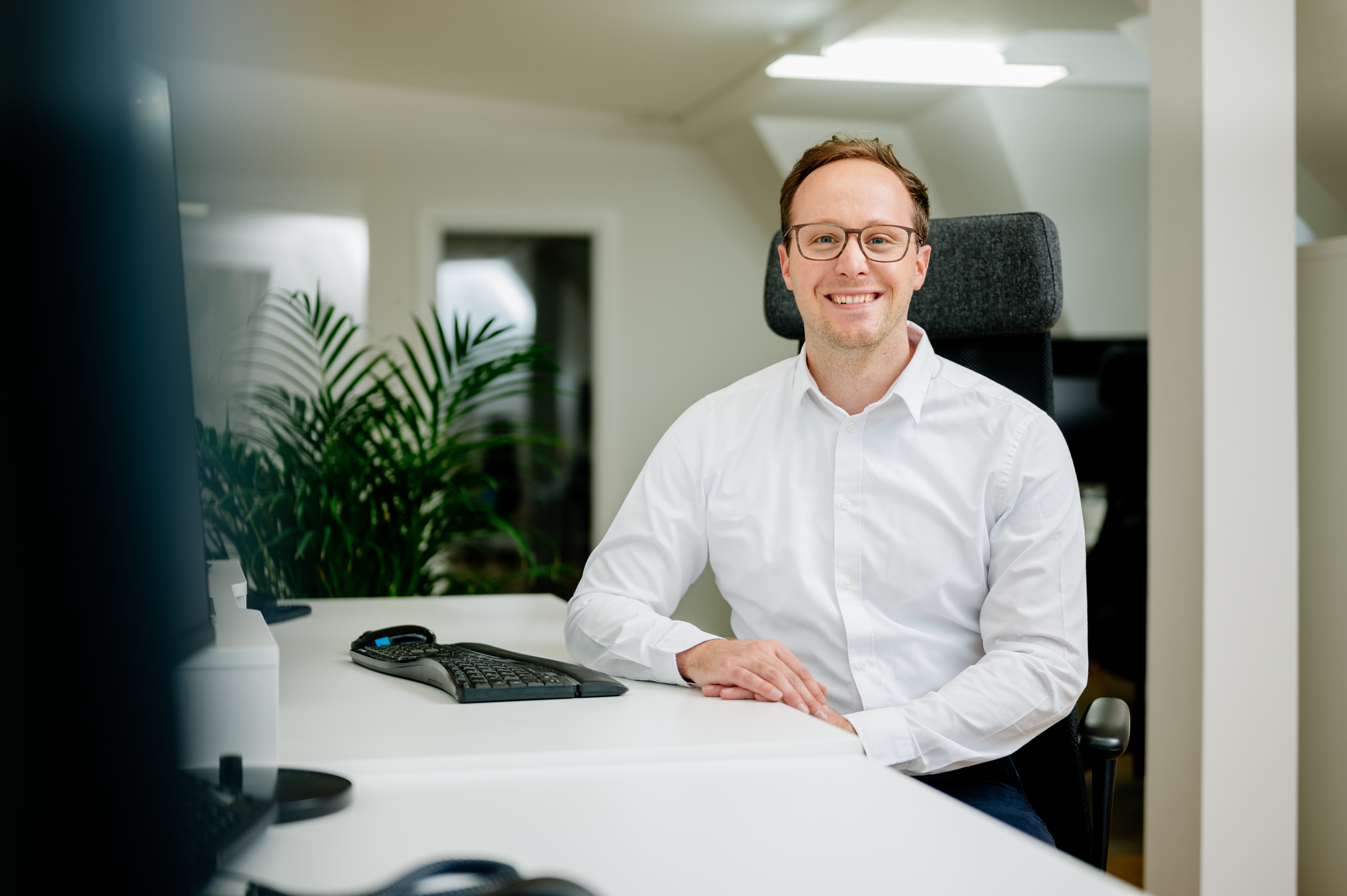 Nino Müns sitzt lächelnd an einem Schreibtisch in einem modernen Büro.