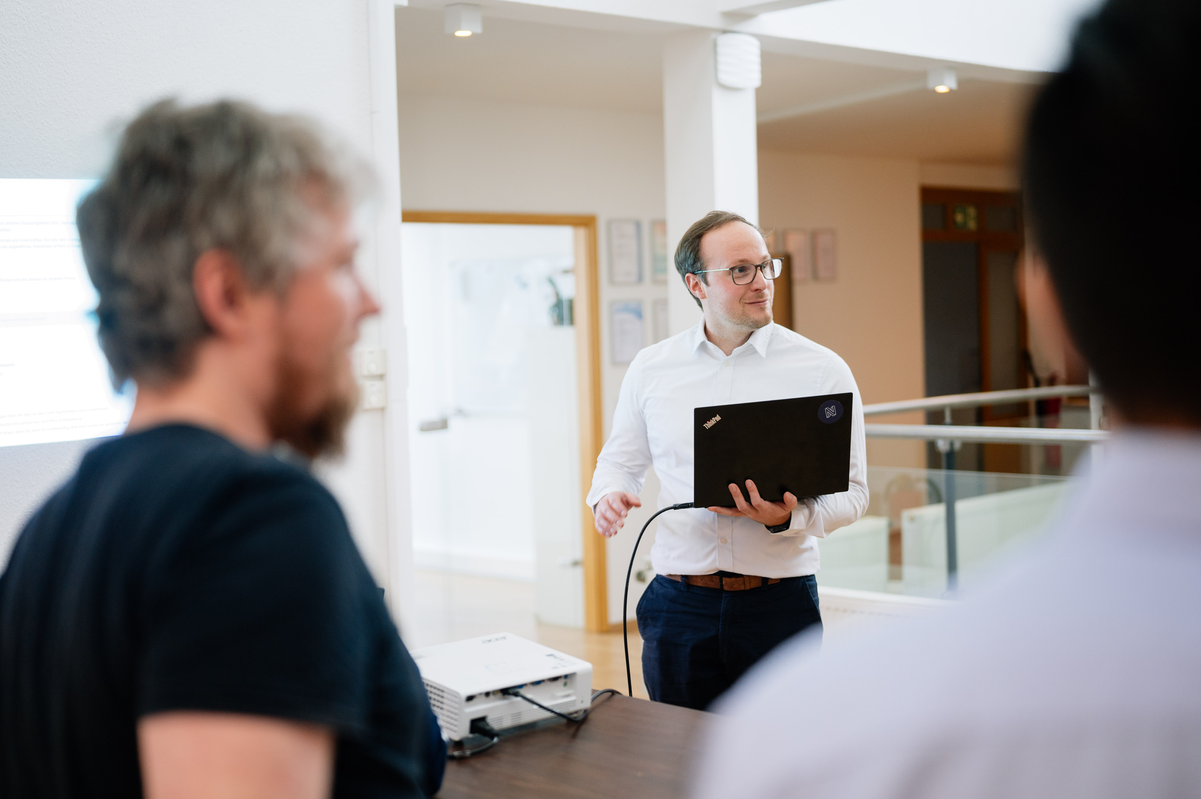 Referent hält einen Vortrag mit Laptop und Beamer vor einer kleinen Gruppe in einem modernen Bürogebäude.